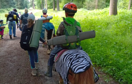 Kind reitet ein Pony mit Zebra-Decke, Wandergruppe im grünen Wald.