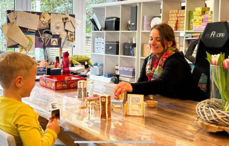 Förderstunde am Tisch: Therapeutin spielt mit Kind, Materialien im Hintergrund.